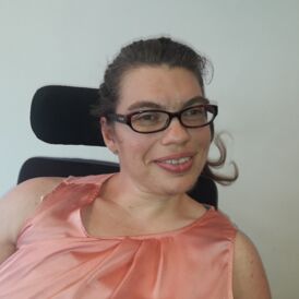 The picture shows Isabella Aigner: a young smiling woman with glasses. Isabella is a wheelchair user.