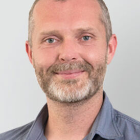 The picture shows Peter Noflatscher. He has short hair, short beard and smiles into the camera.