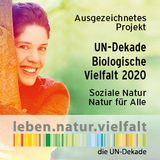 Das ist das Logo des Sonderwettbewerbs „Soziale Natur – Natur für alle“. Damit zeichnet die UN-Dekade beispielhafte Projekte aus, die Natur und Soziales verbinden. Es zeigt eine lächelnde Frau, die einen Baum umarmt.