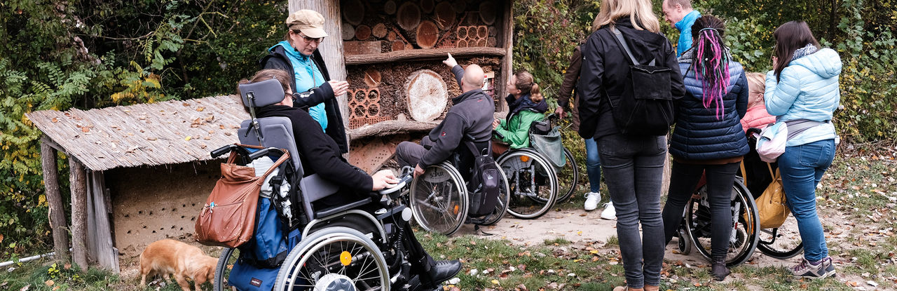 Członkowie zespołu projektu doświadczają poruszania się na wózku inwalidzkim. Widać wiele osób na wózkach i osoby asystujące, dbające o bezpieczeństwo.